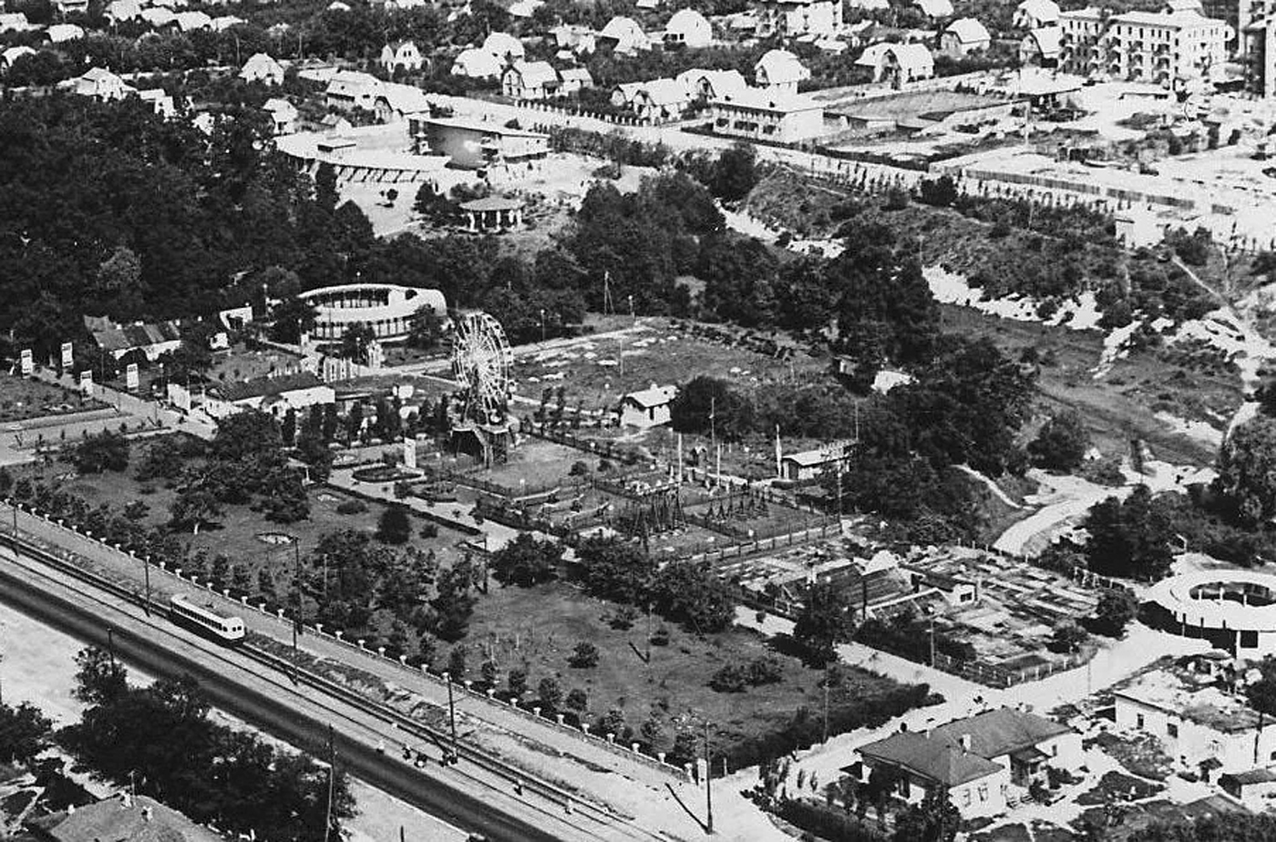 Парк «Ленінського комсомолу». Фото Г. Угриновича другої половини 1950-х років. У парку видно літнє кафе (праворуч) і круглий, просто неба, концертний зал (ліворуч); позаду, за річкою Сирець — велика дерев’яна споруда Зеленого театру. По Брест-Литовському шосе (передній план) проходить трамвайна лінія. На задньому плані — переважно одно-двоповерхова садибна забудова колишнього селища Нивки і вулиця М. Безручка. На Сирці ще не споруджені ставки.